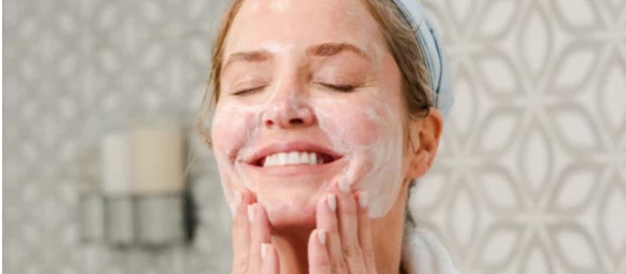 Image of woman applying Age IQ Double Cleansing Face Wash to her face in a bathroom setting.